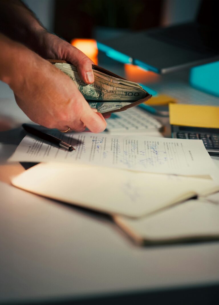 Person handling cash with documents and pen on a desk, suggesting financial management.
